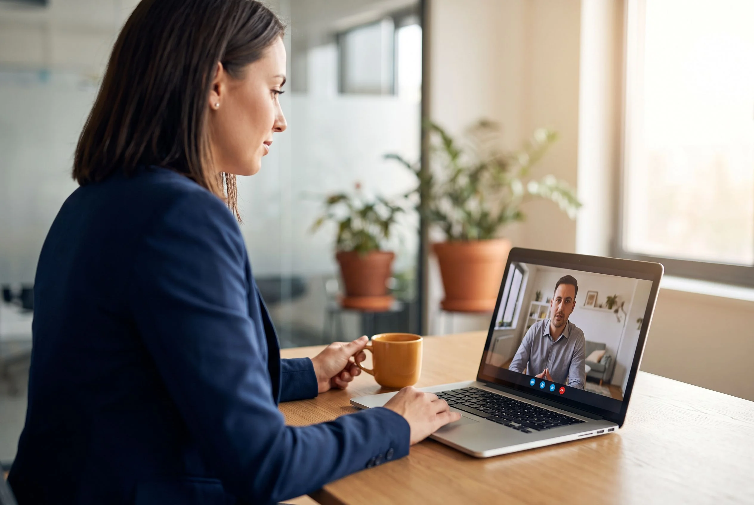 HR manager video calling a nearshore data engineering candidate in a modern office, orange accent coffee mug on desk