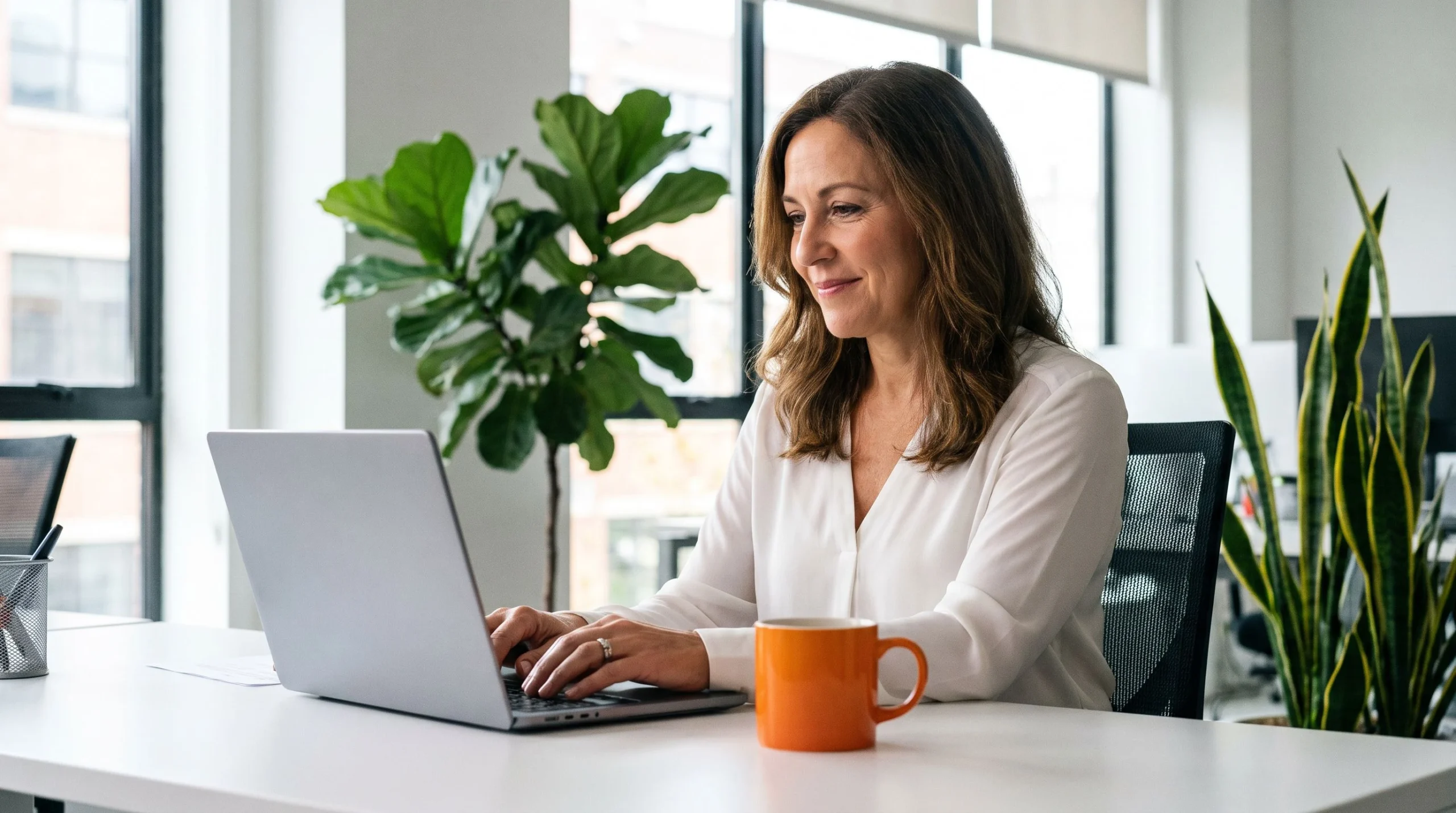 HR professional drafting a customer service representative job description on a laptop with orange coffee mug