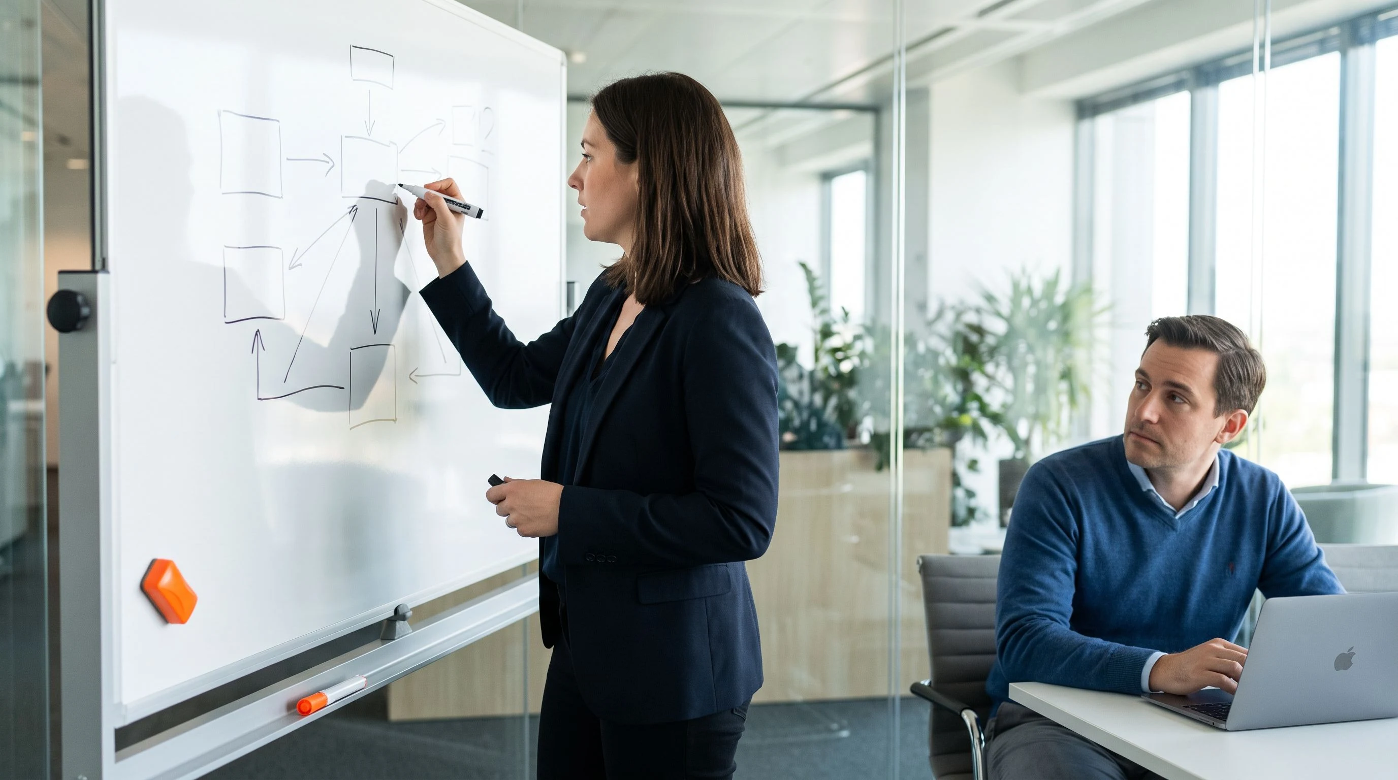 Candidate whiteboarding a systems integration diagram during a technical interview, warm orange marker cap visible on the desk