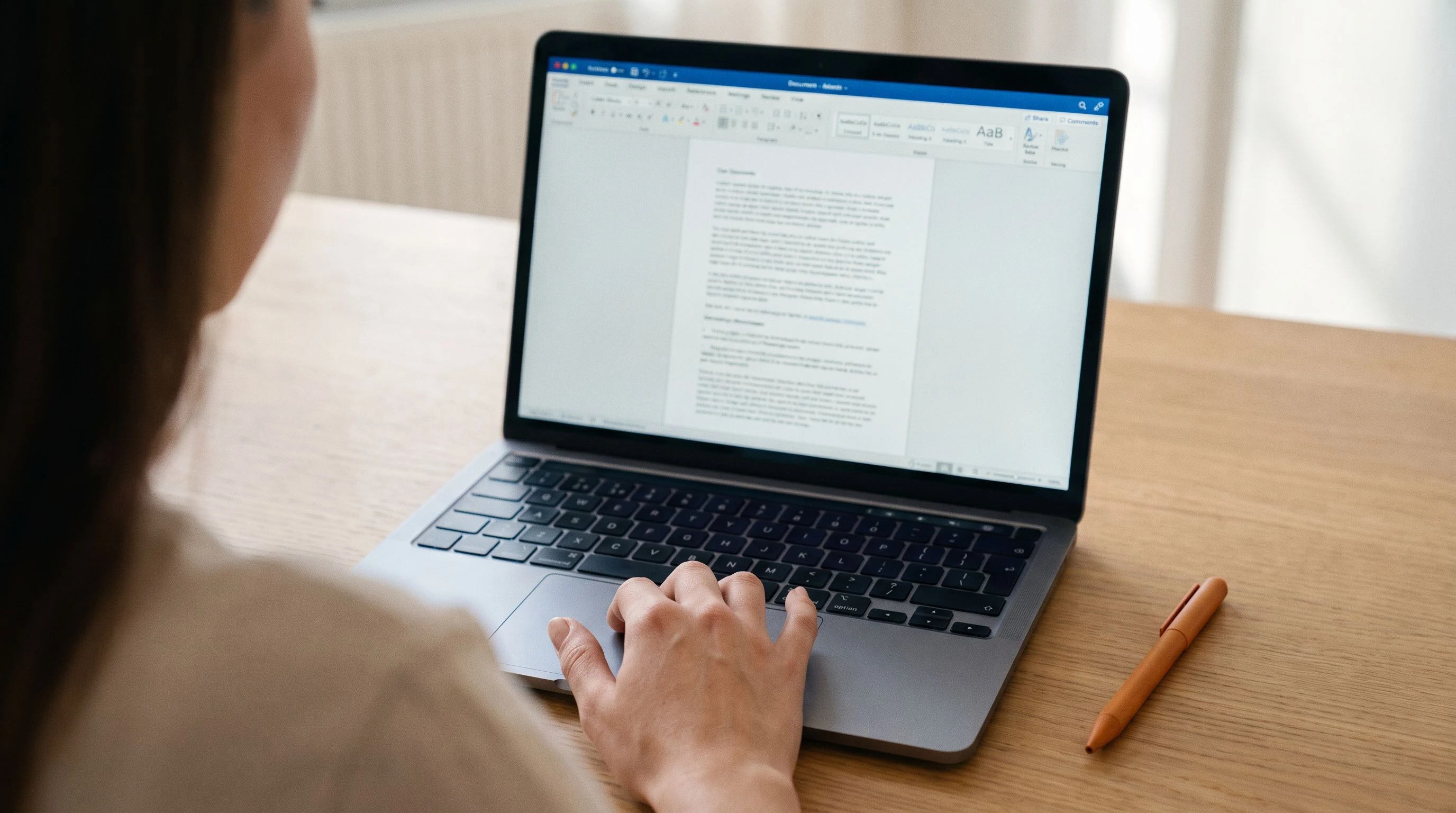 Close-up of a laptop screen showing a finished job description document being reviewed, warm orange highlighter on the desk