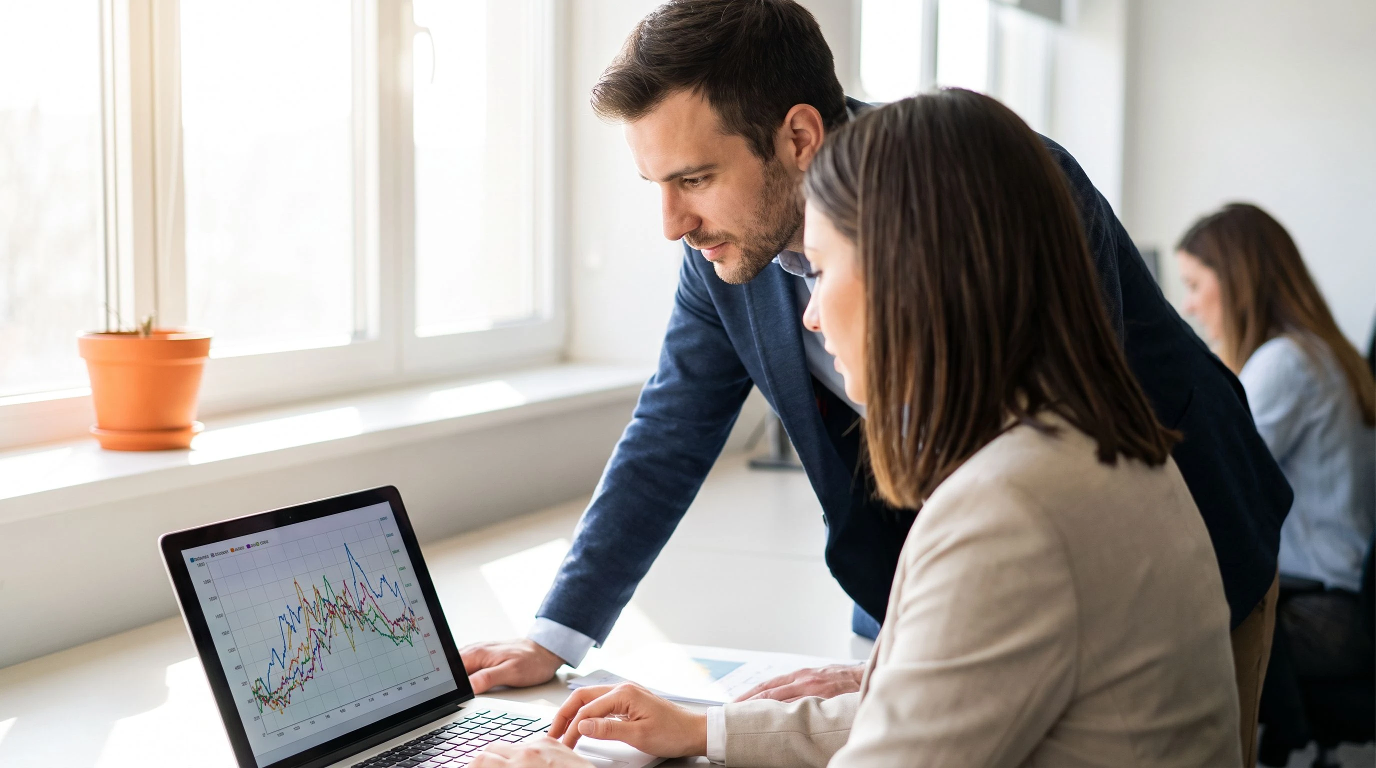 Two engineers reviewing SwiftUI code and a memory profiling chart on a laptop in a well-lit office, small orange plant pot on the windowsill