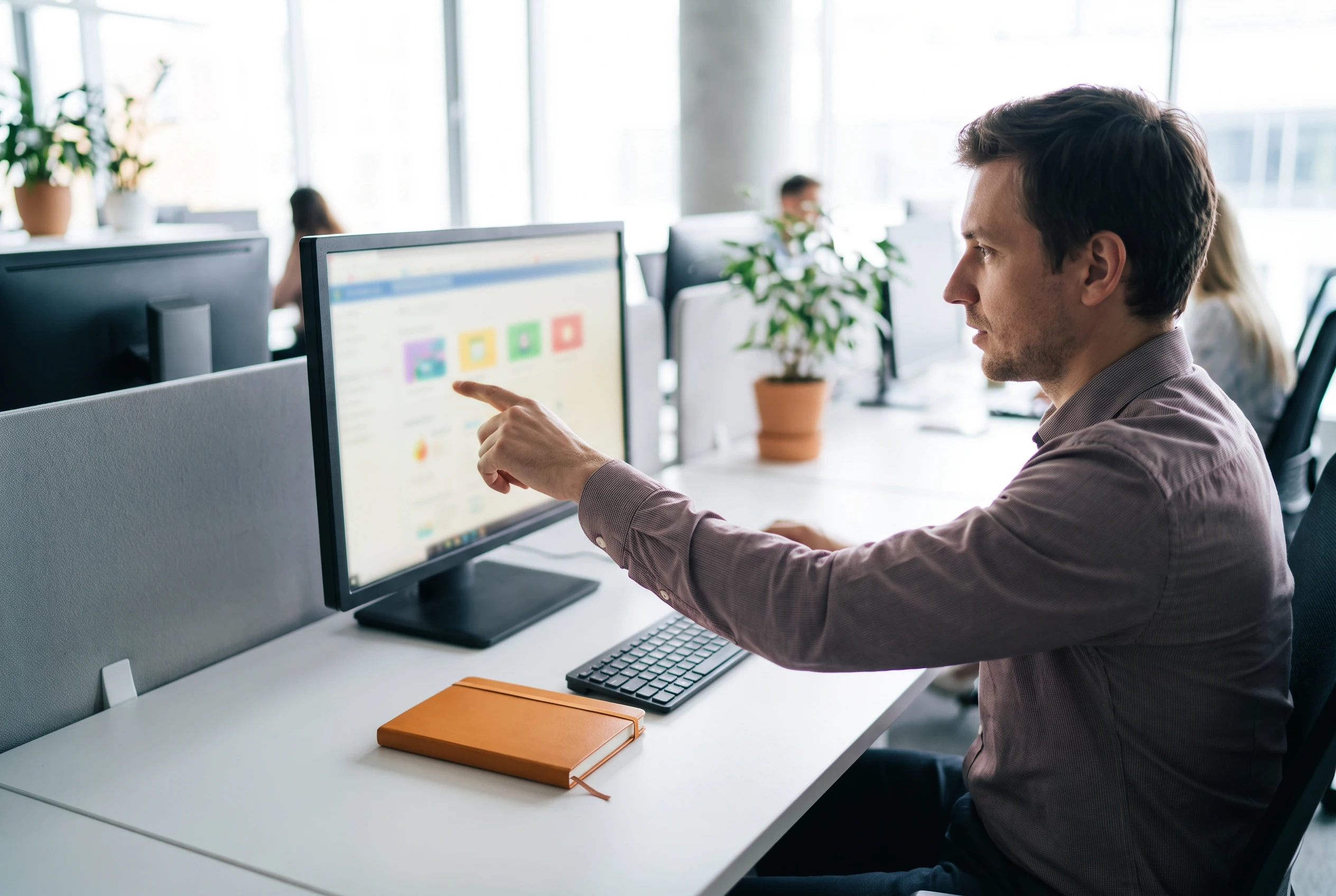 IT support specialist pointing at a colleague's monitor while resolving an internal software issue