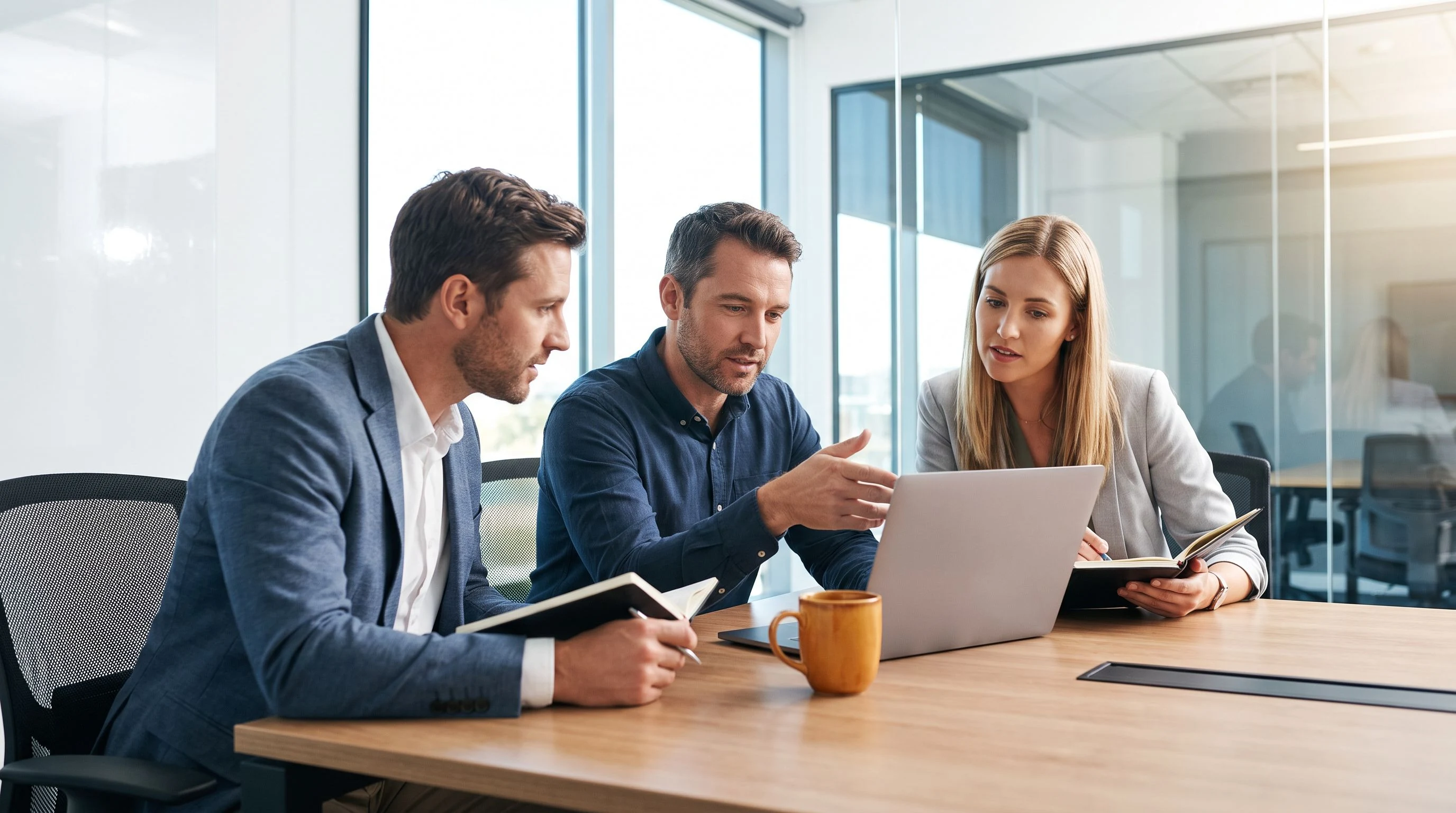 Technical interview panel discussing a candidate around a table with laptops, orange accent detail