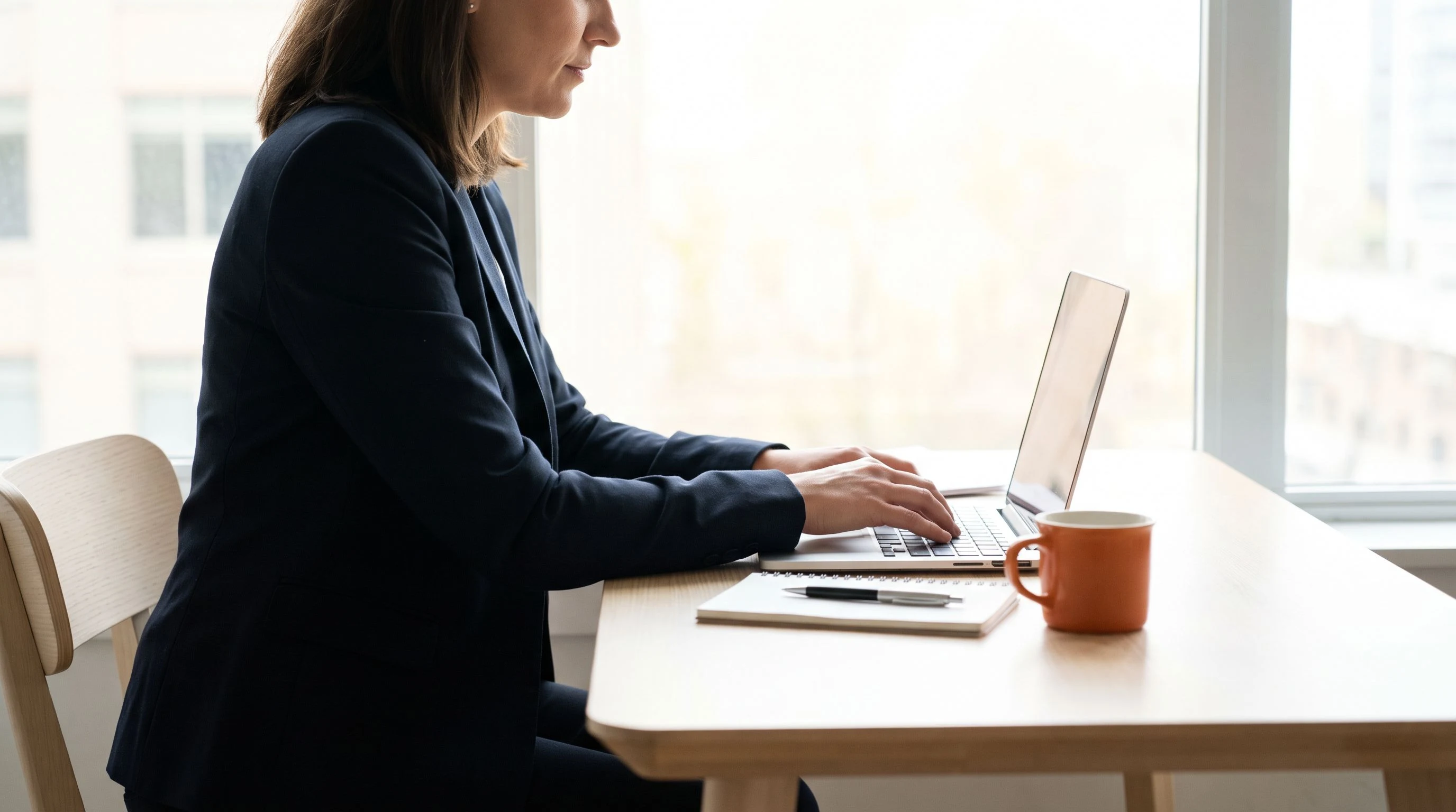 Hiring manager drafting a job description on a laptop at a desk, orange accent detail
