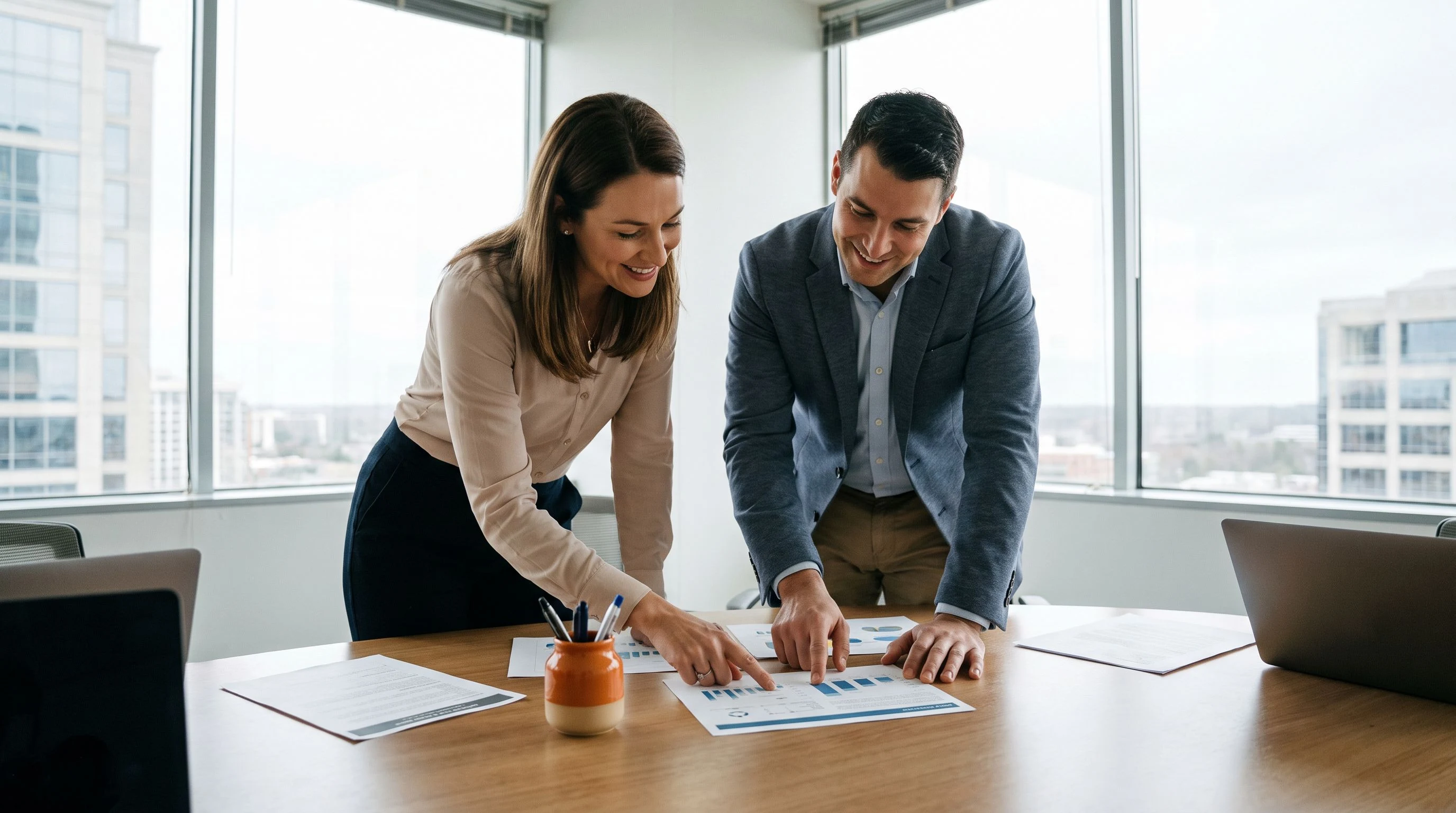 HR director and hiring manager reviewing printed candidate screening documents at a meeting table in a modern office