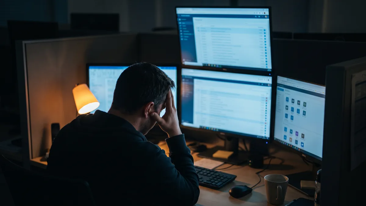 Single in-house IT help desk technician working alone late at night with a backed-up ticket queue