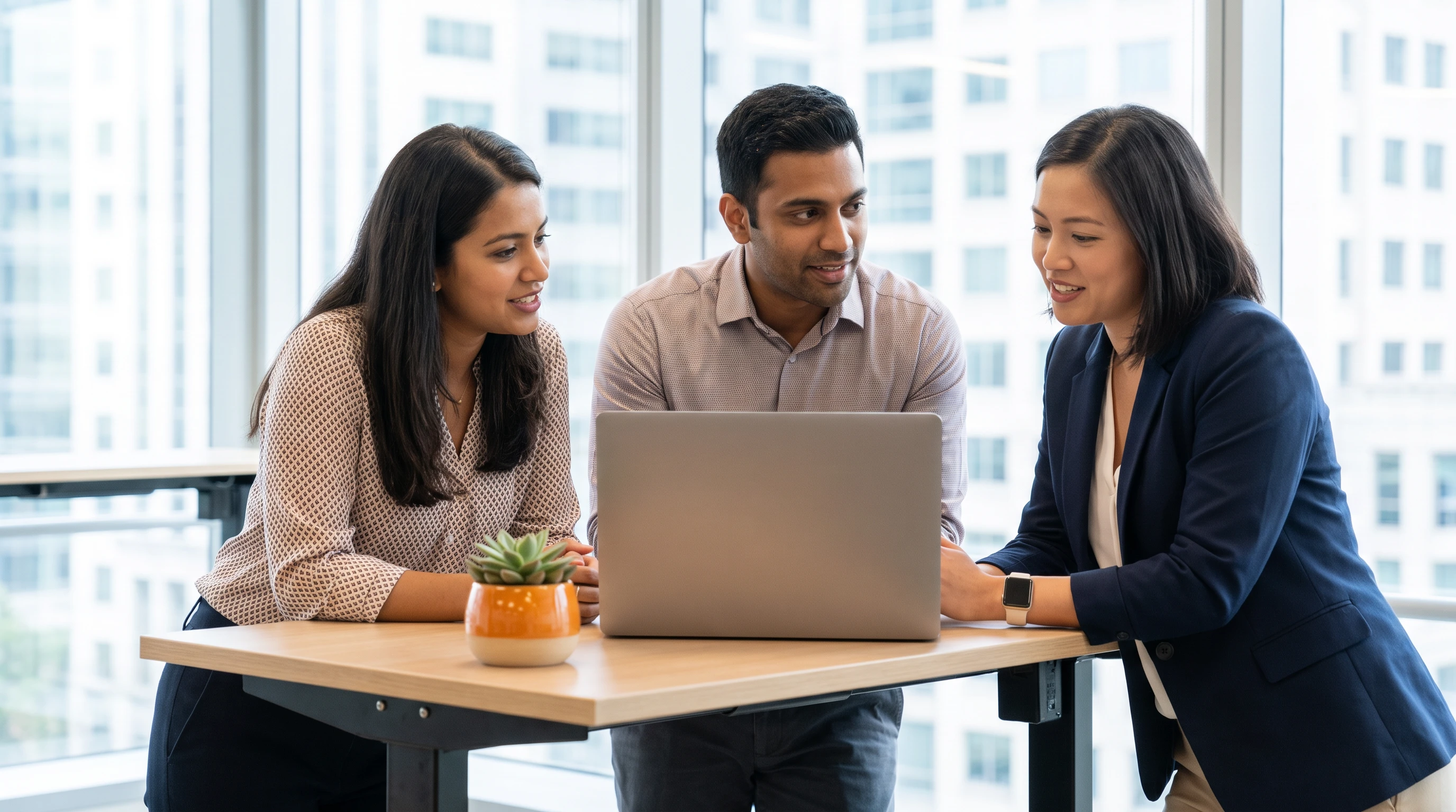 Three colleagues collaborating closely around a laptop on a standing desk